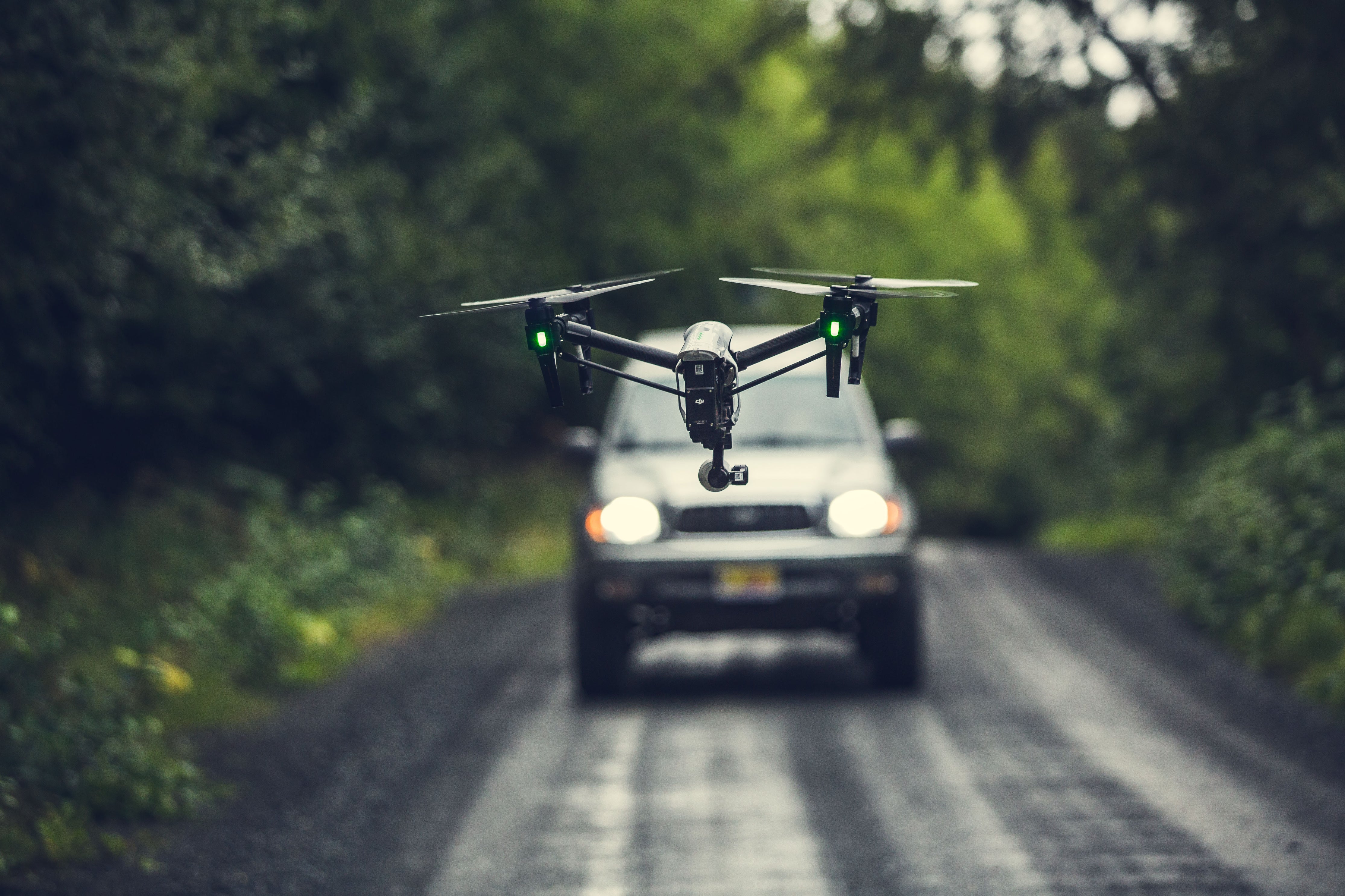 A drone flying over road with a car behind it.